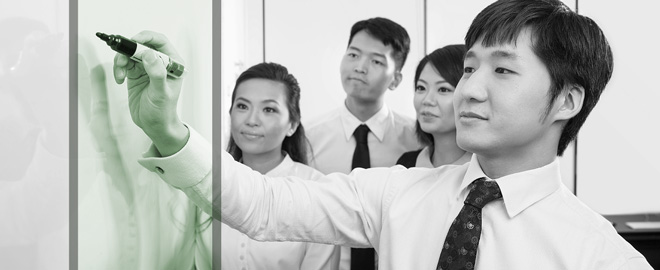 Chinese man writing on whiteboard with colleagues